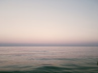 Wide landscape shot of a calm sea meeting a pale horizon under a gentle sky.