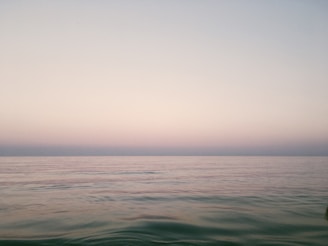 Wide landscape shot of a calm sea meeting a pale horizon under a gentle sky.