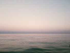 A serene seascape with calm water meeting the horizon under a soft gradient sky transitioning from pale orange to light blue.