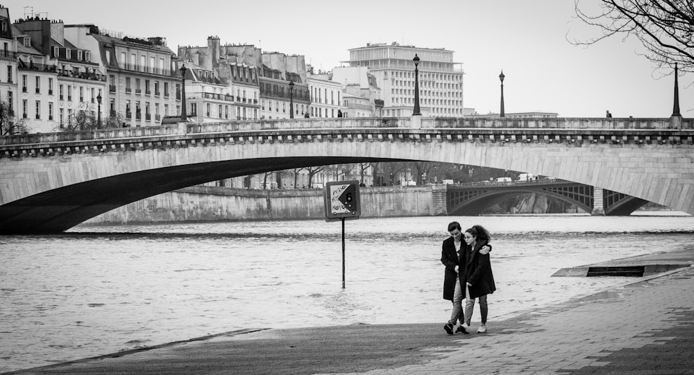 grayscale photo of man and woman walking on bridge
