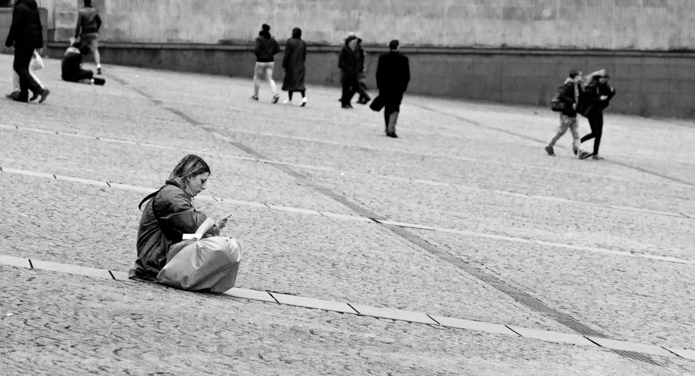 grayscale photo of woman in black jacket and pants sitting on ground