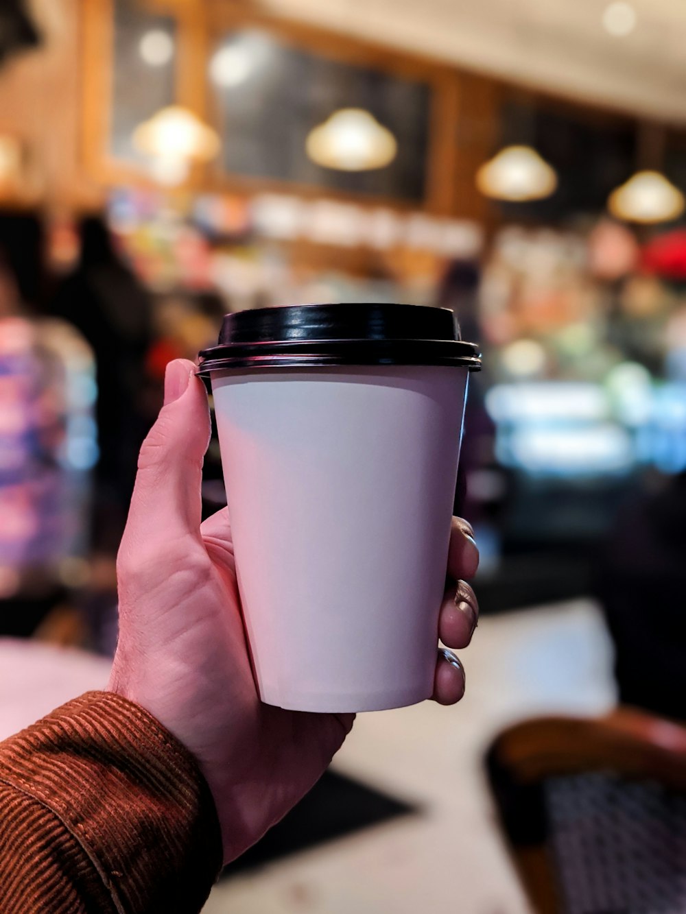 Persona che tiene la tazza usa e getta bianca e nera