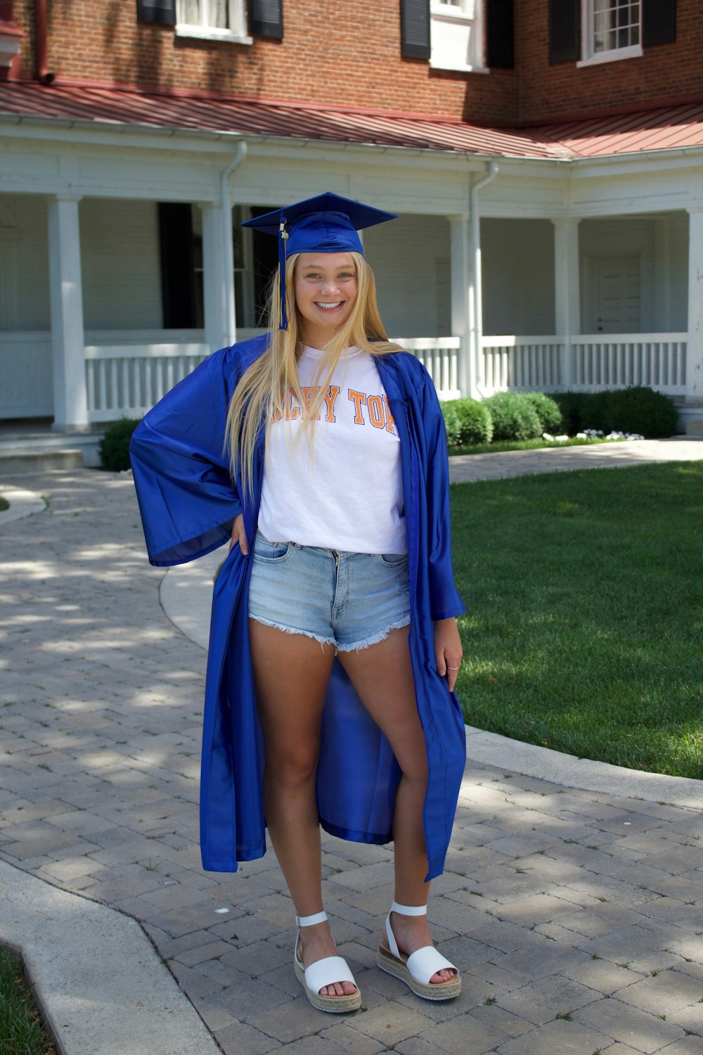 woman in blue academic dress standing on gray asphalt road during daytime