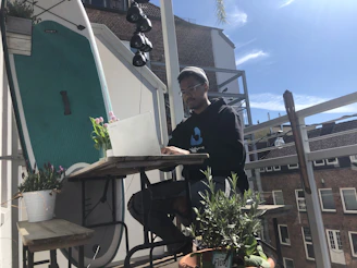 A cheerful traveler using a laptop to book a vacation on a sunny balcony.