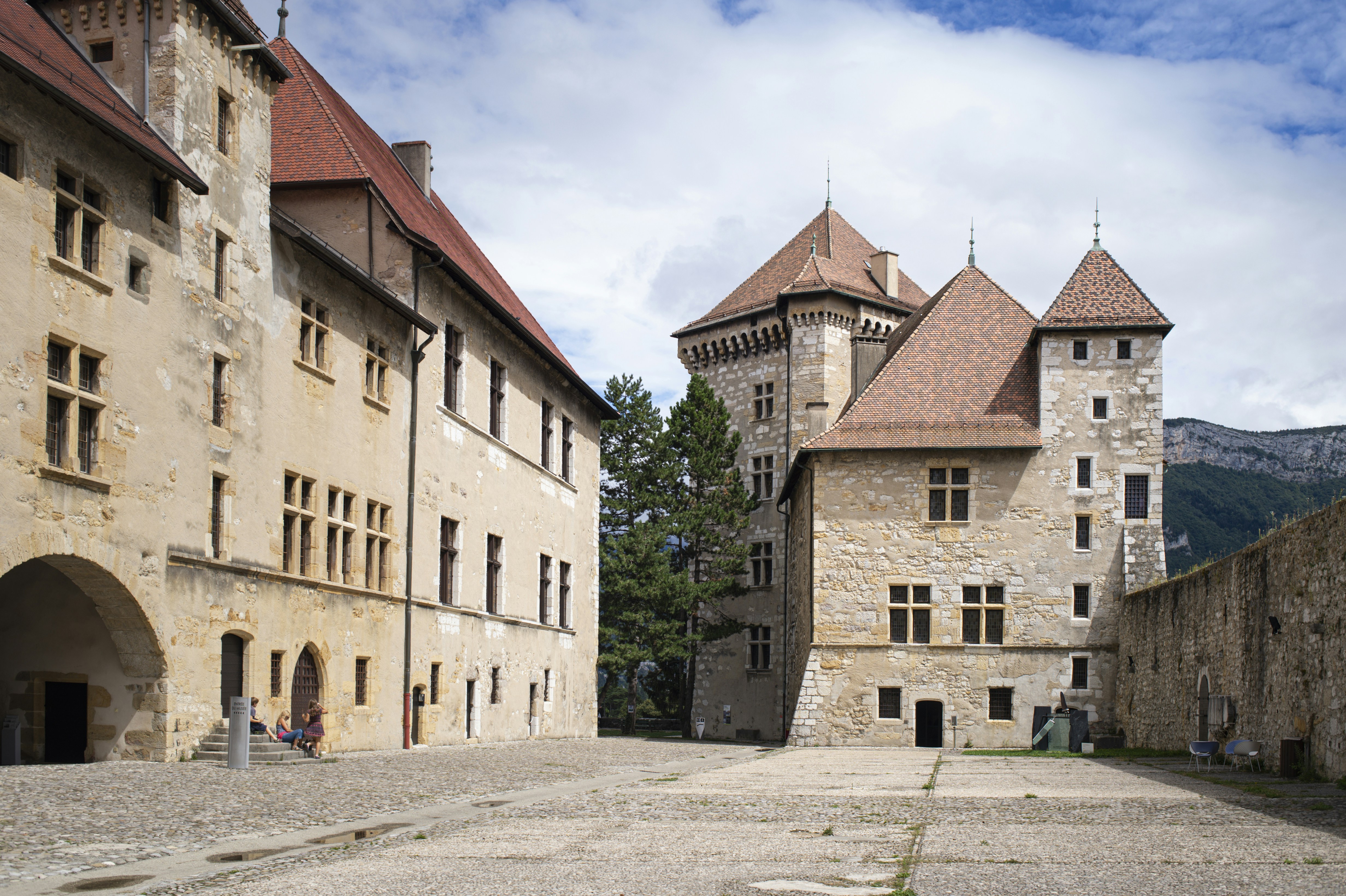 brown and white concrete building under white clouds during daytime, Inside courtyard of a medieval castle Annecy Château.