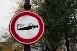 A round traffic sign with a red border against a backdrop of trees and poles. Inside the sign is an image of a hand holding a bottle with the text '% ALC' printed on it.