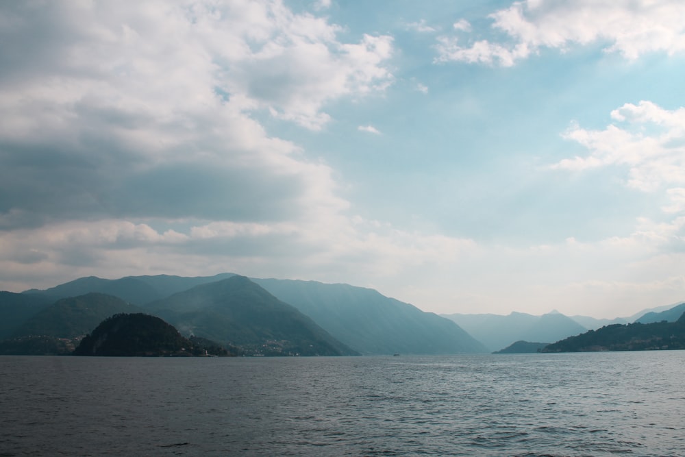 body of water near mountain under cloudy sky during daytime