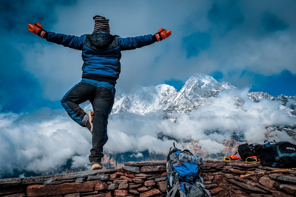 man in blue jacket and blue denim jeans standing on rock formation under white clouds during