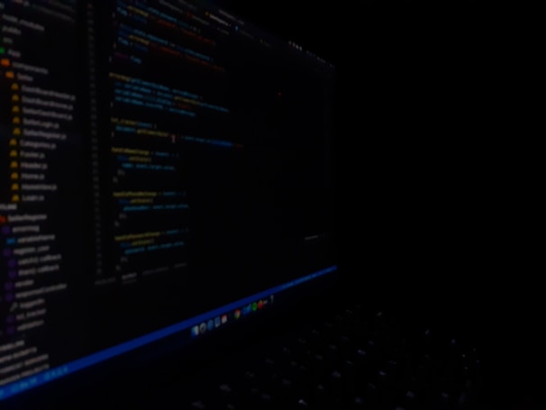 A close-up view of a computer screen displaying code in a dark setting. The code appears to be written in a text editor with syntax highlighting, featuring various lines of text and numbers. The surroundings are dimly lit, emphasizing the bright screen against the dark background.