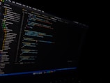 A computer screen displaying a code editor with visible syntax highlighting. The editor shows various files listed on the left panel and a JavaScript file open with lines of code visible. The environment appears to be a dark-themed setting.