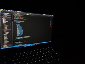 A sleek laptop displaying code on the screen with a glowing keyboard in a dark setting.