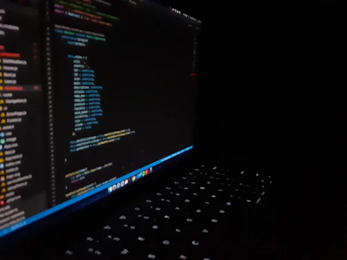 A sleek dark-themed illustration of a laptop with cloud and code icons floating around it.