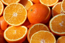 A close-up view of several whole and halved oranges with vibrant orange peel and juicy segments, showcasing freshness and nutrition.