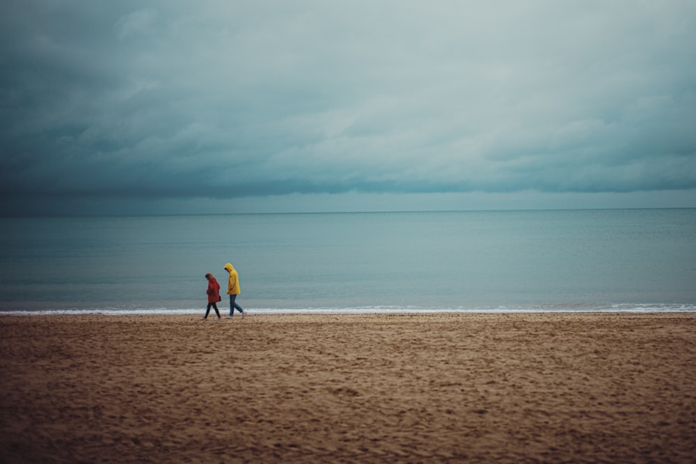 2 pessoa andando na areia marrom perto do corpo de água durante o dia