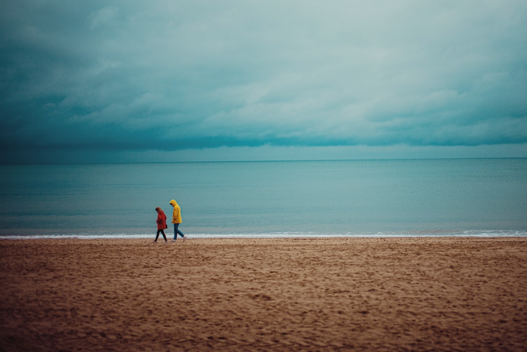 2 person walking on brown sand near body of water during daytime