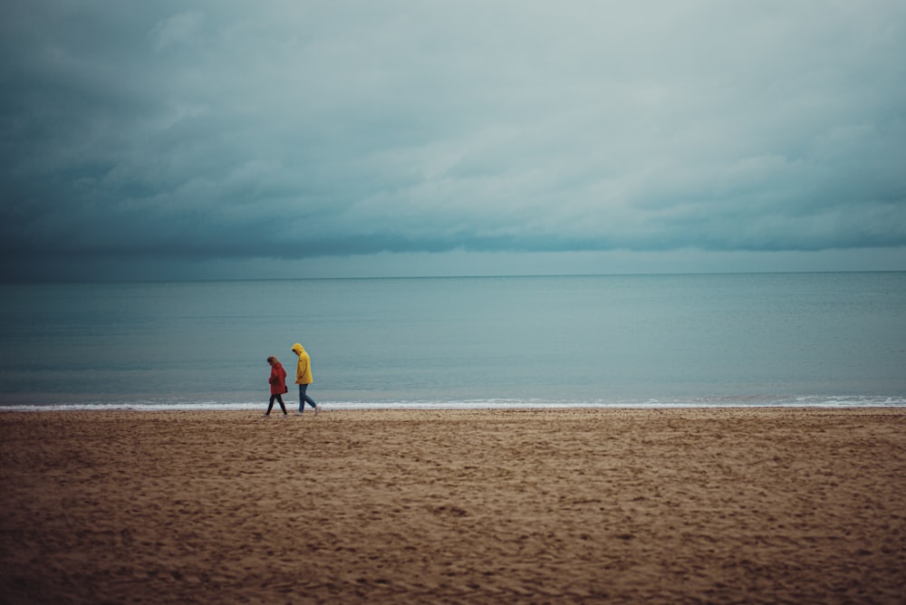 2 person walking on brown sand near body of water during daytime