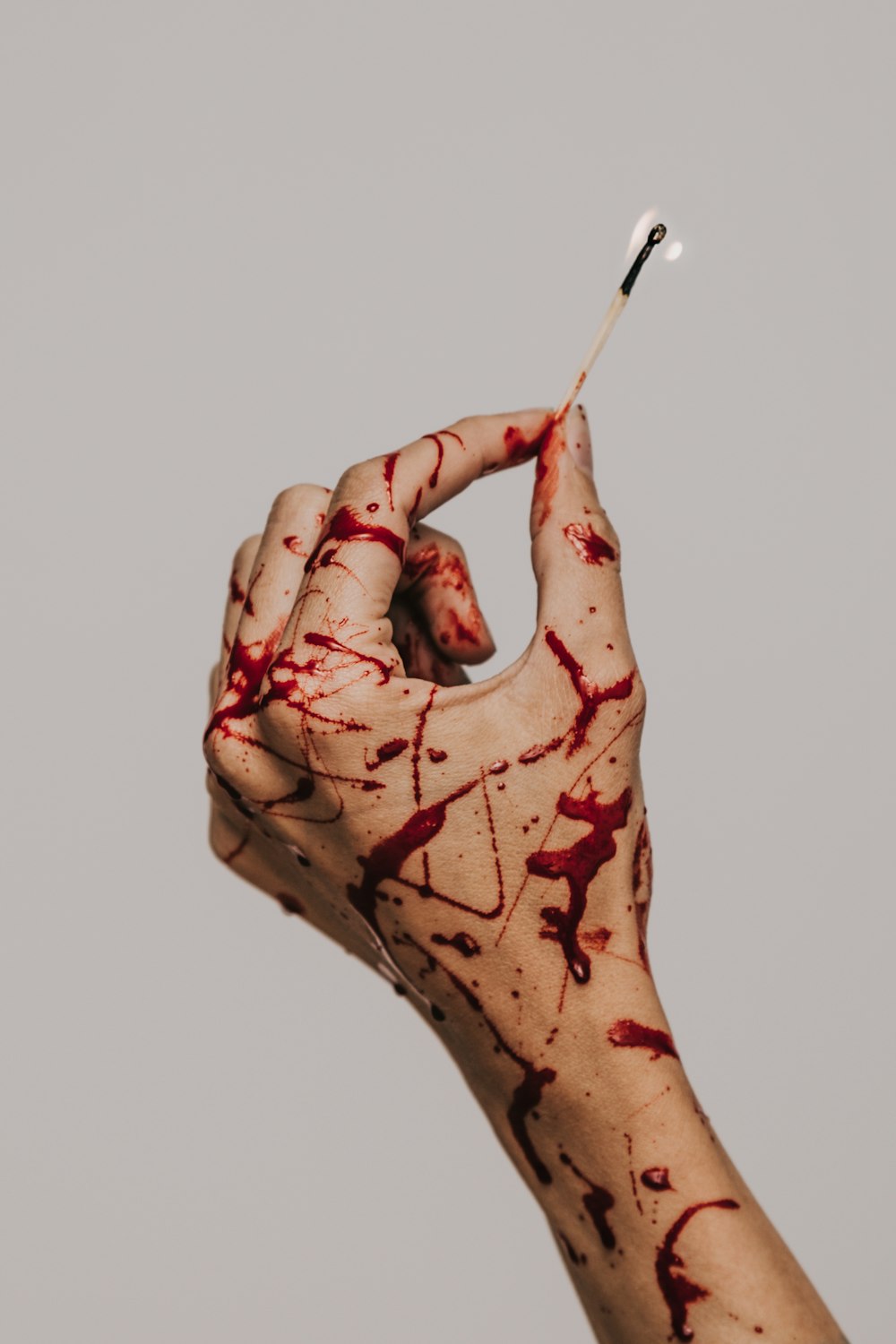 Una mano cubierta de salpicaduras de sangre sosteniendo un fósforo encendido