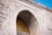 A detailed stone arch with intricate Arabic calligraphy in gold is featured. The arch is adorned with carvings of a crescent moon and star, symbols commonly associated with Islam. The building is constructed from light-colored stone with ornate details, reflecting traditional Islamic architectural elements.