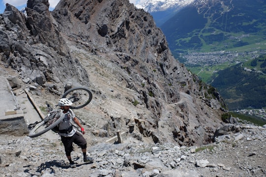 man in black jacket and gray pants carrying black backpack walking on rocky mountain during daytime in Bormio Italy