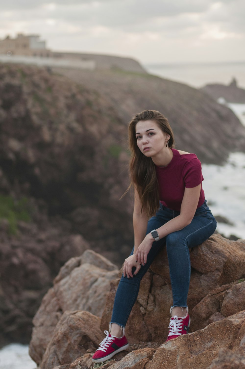 woman in red shirt and blue denim jeans sitting on brown rock during daytime