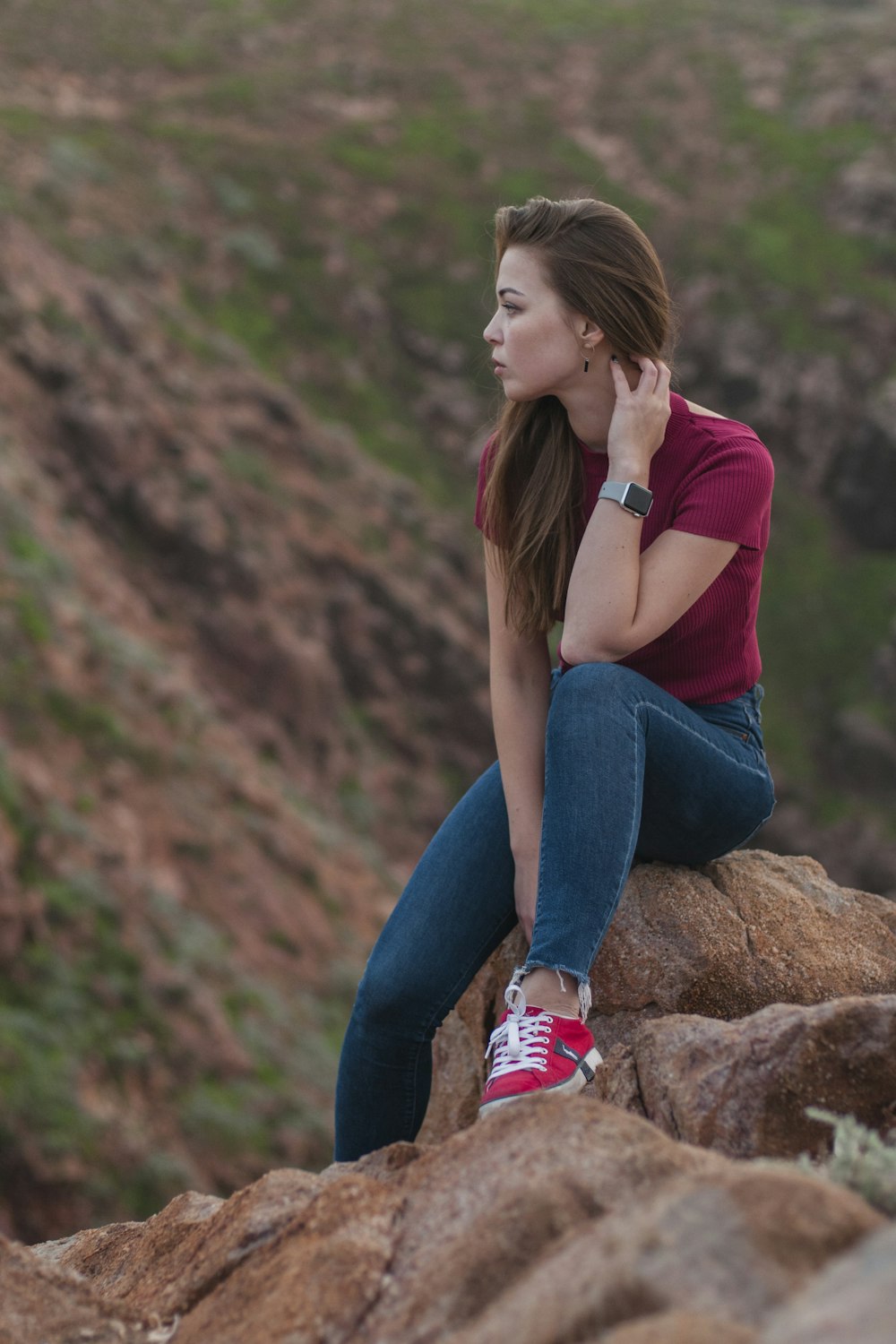 woman in pink shirt and blue denim jeans sitting on brown rock during daytime