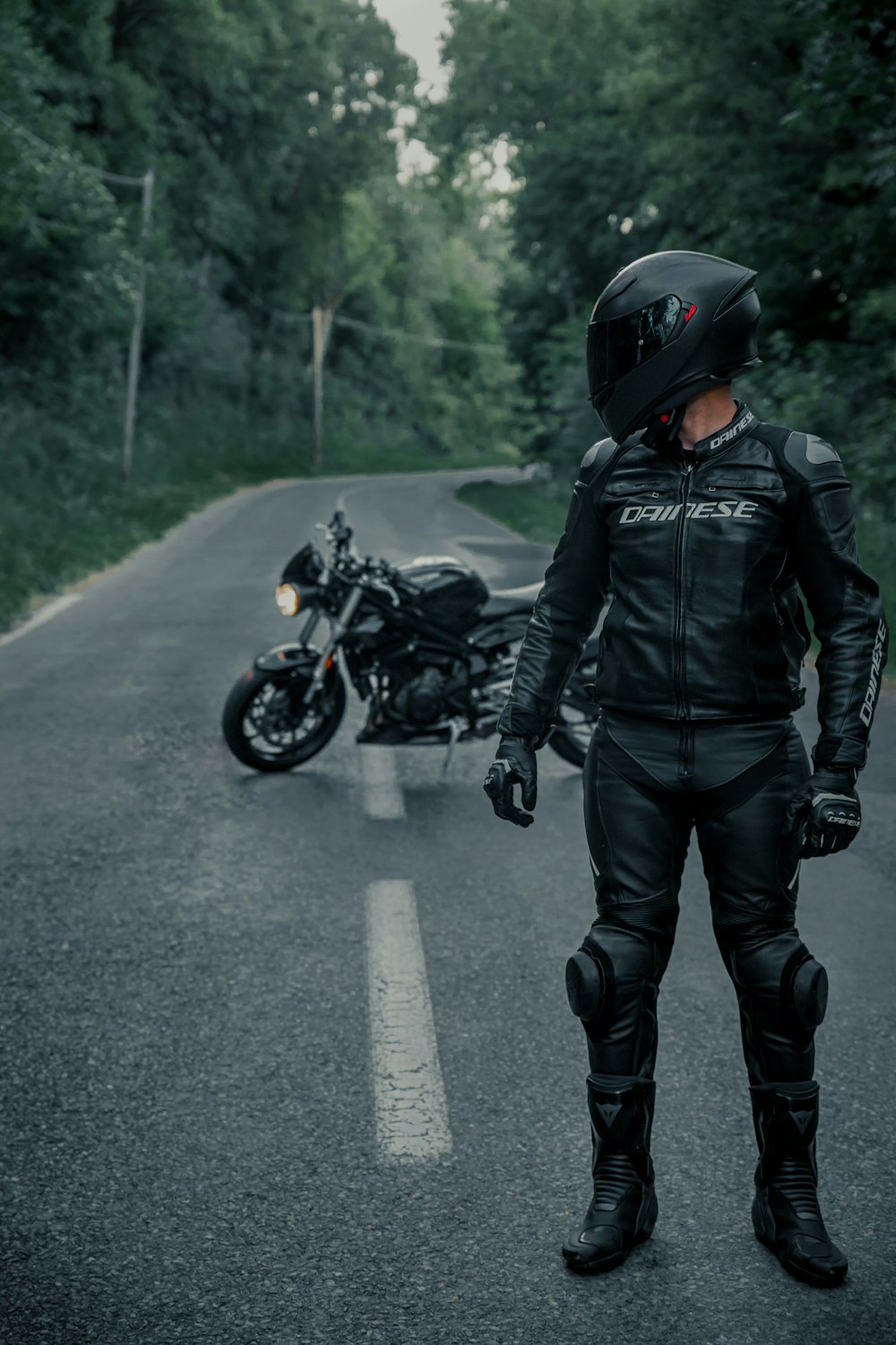 黒い革のジャケットと黒いヘルメットをかぶった男が昼間、道路でバイクに乗っている