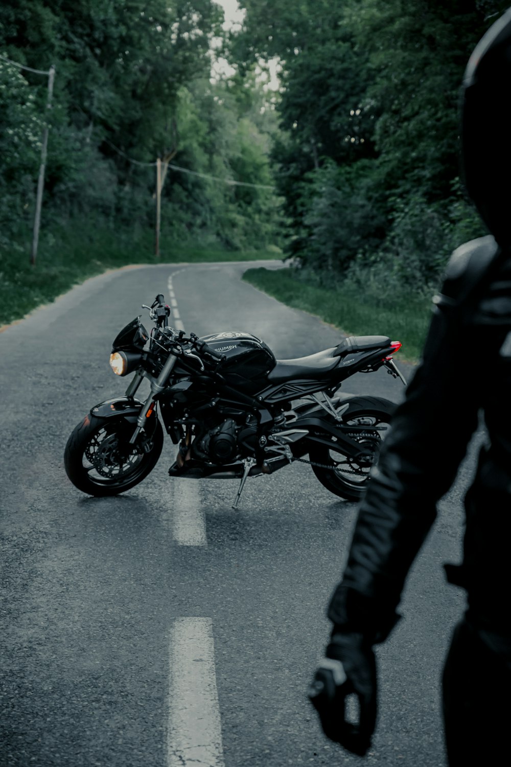 Mann in schwarzer Jacke und schwarzer Hose fährt tagsüber schwarzes Motorrad auf der Straße