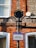 A street sign is mounted on a post against a brick building. The sign indicates a taxi stand for seven taxis, available 24 hours, with 'Wantage' written above it. The wall is predominantly made of red and black bricks and features windows with white frames.