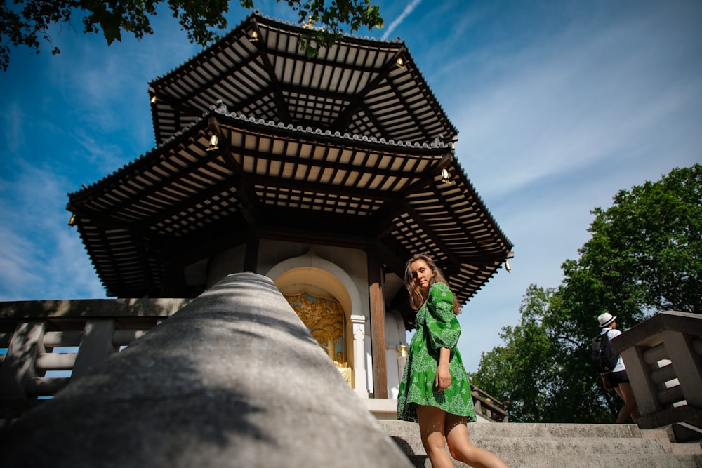 woman in green dress standing near brown wooden house during daytime