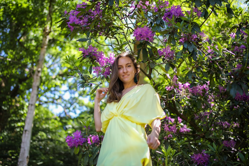 woman in yellow dress standing beside purple flowers during daytime