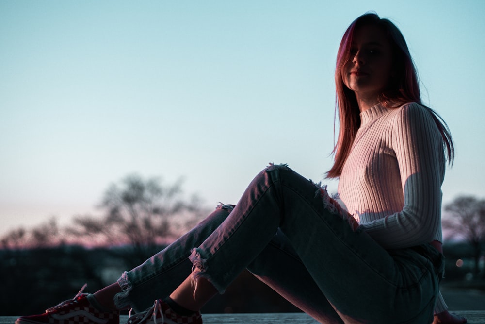 woman in white and brown striped shirt and blue denim jeans sitting on brown wooden fence