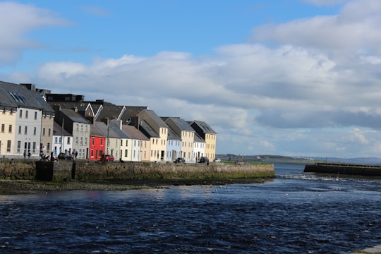 white and brown concrete building beside body of water under blue sky during daytime in Claddagh Ireland