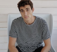man in black and white striped crew neck t-shirt sitting on white plastic chair
