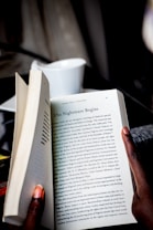 A person holds open a book, revealing a page with the title 'The Nightmare Begins.' The text discusses historical and political events. The person's fingers are visible, and a white cup is blurred in the background.