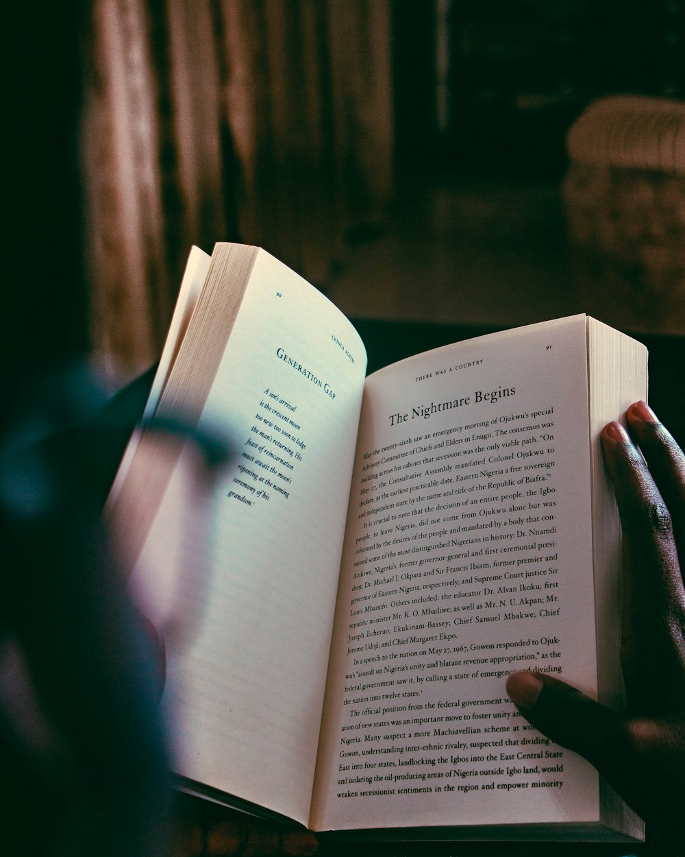 person reading book on brown woven chair