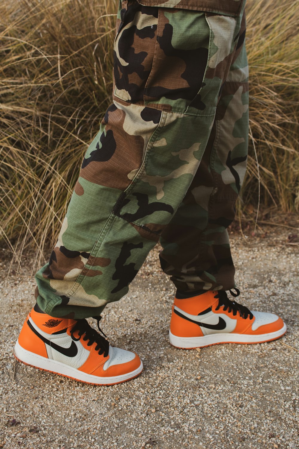 person in green brown and black camouflage pants and orange nike sneakers