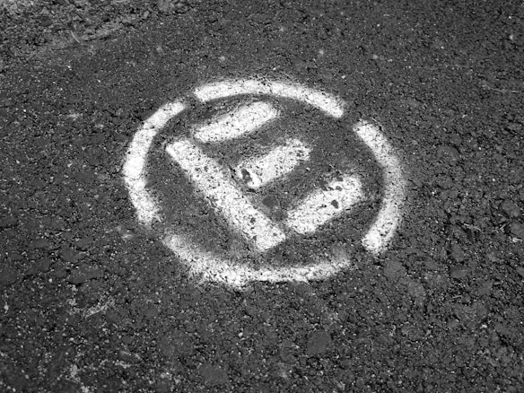 A textured surface with a white spray-painted no parking symbol, featuring a large letter 'P' crossed out within a circle.