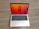 A laptop with a sleek silver finish is open on a wooden surface. Its screen displays a vibrant orange and red abstract floral wallpaper, and several application icons are visible on the desktop. The keyboard features a black background with white letters, and the laptop appears to be a compact model.