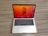A laptop with a sleek silver finish is open on a wooden surface. Its screen displays a vibrant orange and red abstract floral wallpaper, and several application icons are visible on the desktop. The keyboard features a black background with white letters, and the laptop appears to be a compact model.