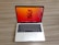 A laptop with a sleek silver finish is open on a wooden surface. Its screen displays a vibrant orange and red abstract floral wallpaper, and several application icons are visible on the desktop. The keyboard features a black background with white letters, and the laptop appears to be a compact model.