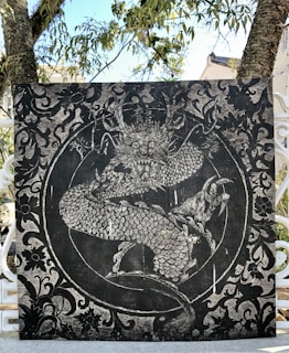 A detailed artwork features a majestic dragon entwined in a circular pattern surrounded by ornate decorations and foliage. The texture is monochrome with intricate line work and shading.