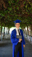man in blue academic dress and academic hat standing near green tree during daytime