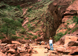 woman in blue shirt and blue denim jeans standing on brown rocky mountain during daytime