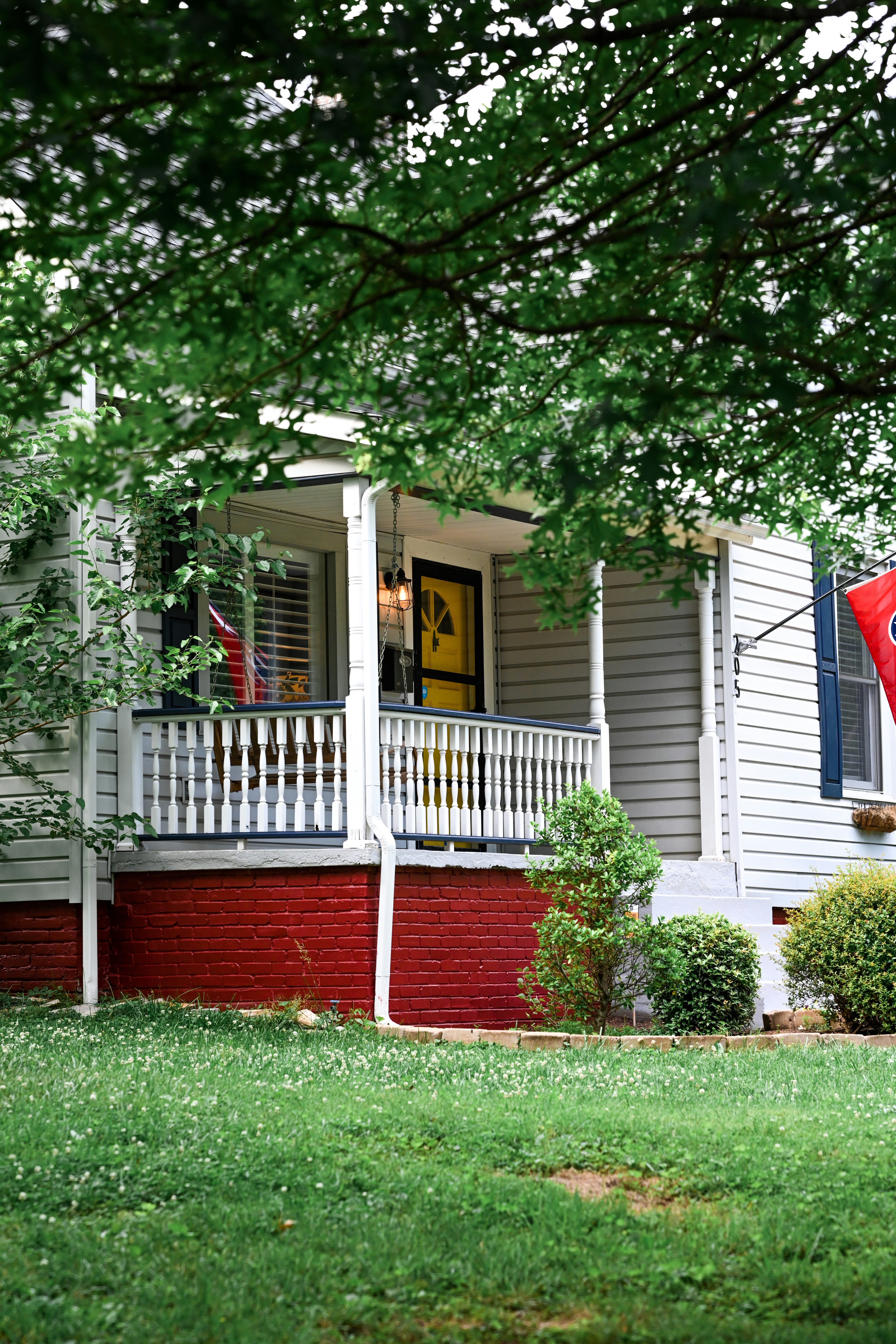 A charming house with a yellow front door and red brick base, surrounded by greenery.