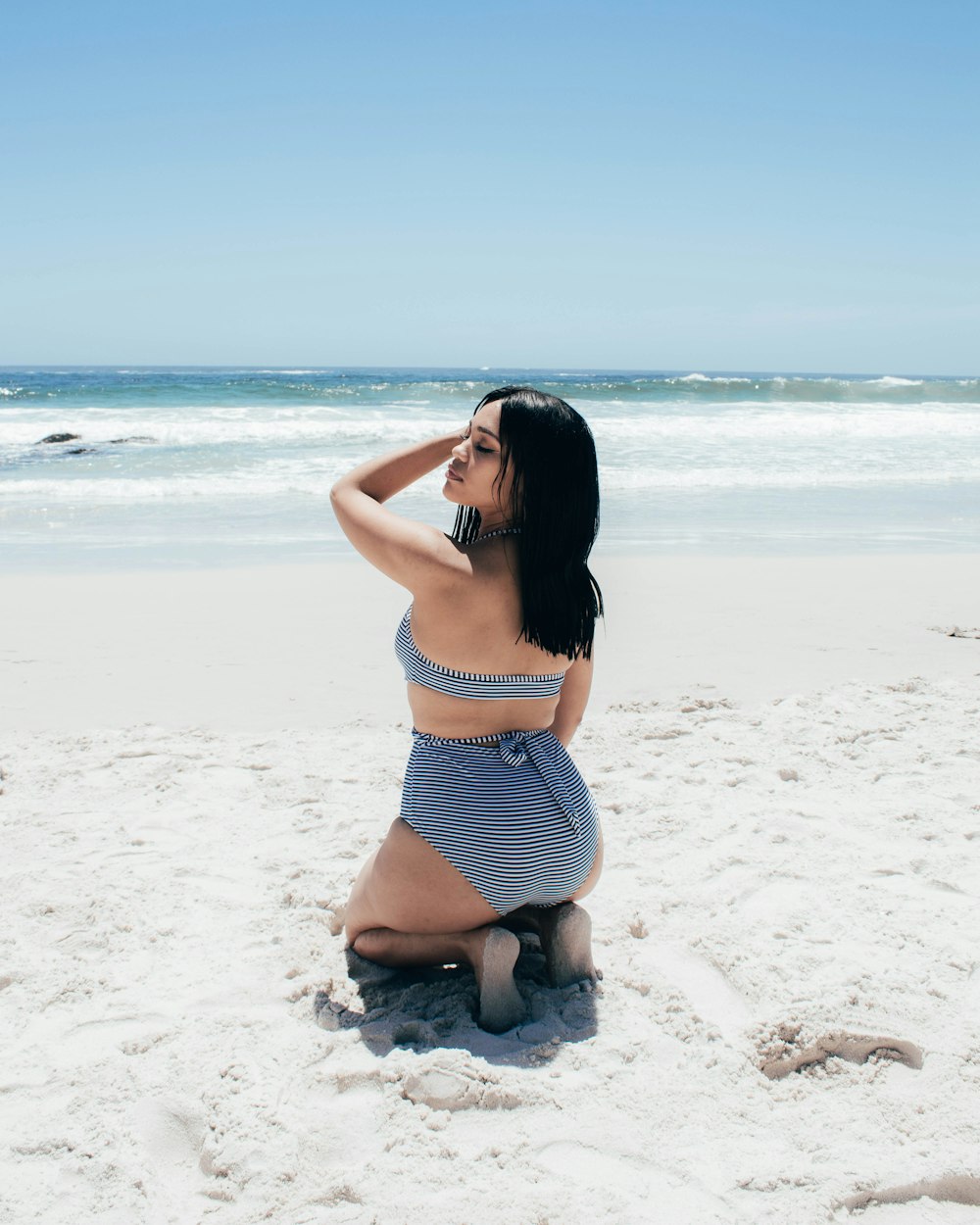 mulher no biquíni listrado azul e branco na praia durante o dia