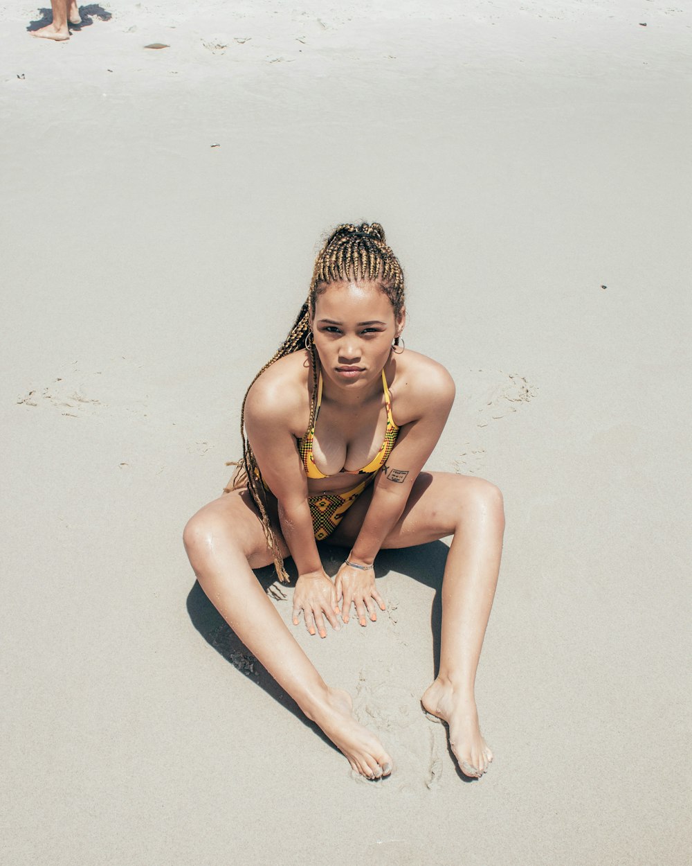 femme en bikini jaune assis sur le sable pendant la journée