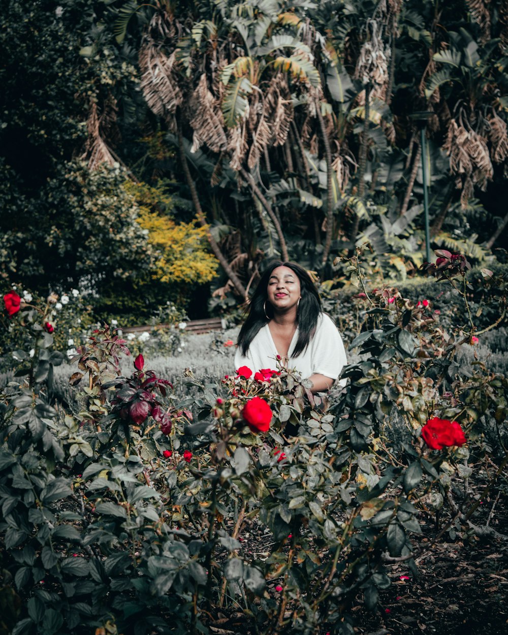 woman in white long sleeve shirt standing beside red flowers