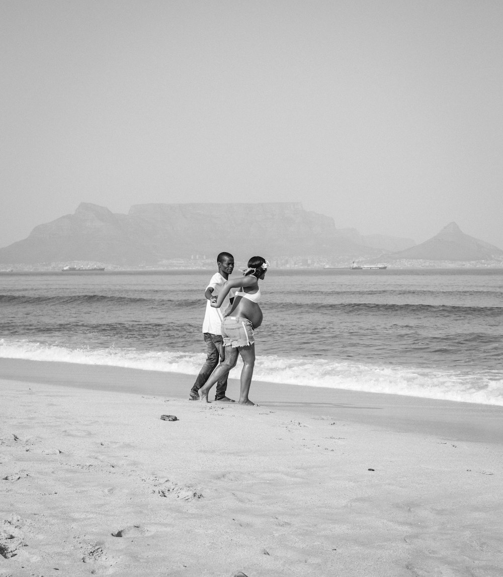 grayscale photo of couple walking on beach