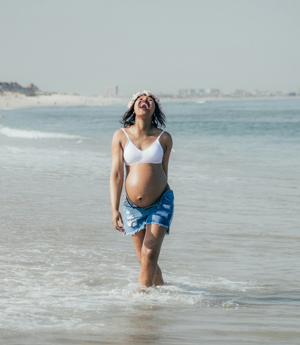 Woman in white sports bra and blue denim shorts standing on beach