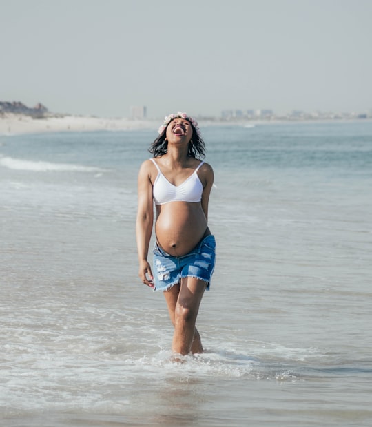 woman in white sports bra and blue denim shorts standing on beach during daytime in Bloubergstrand South Africa